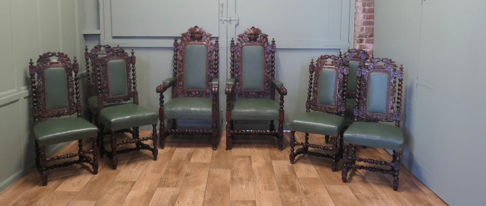 A set of ten carved oak dining chairs featuring green leather upholstery, barley twist legs, and detailed crest rails, comprising two carver armchairs and eight side chairs.
