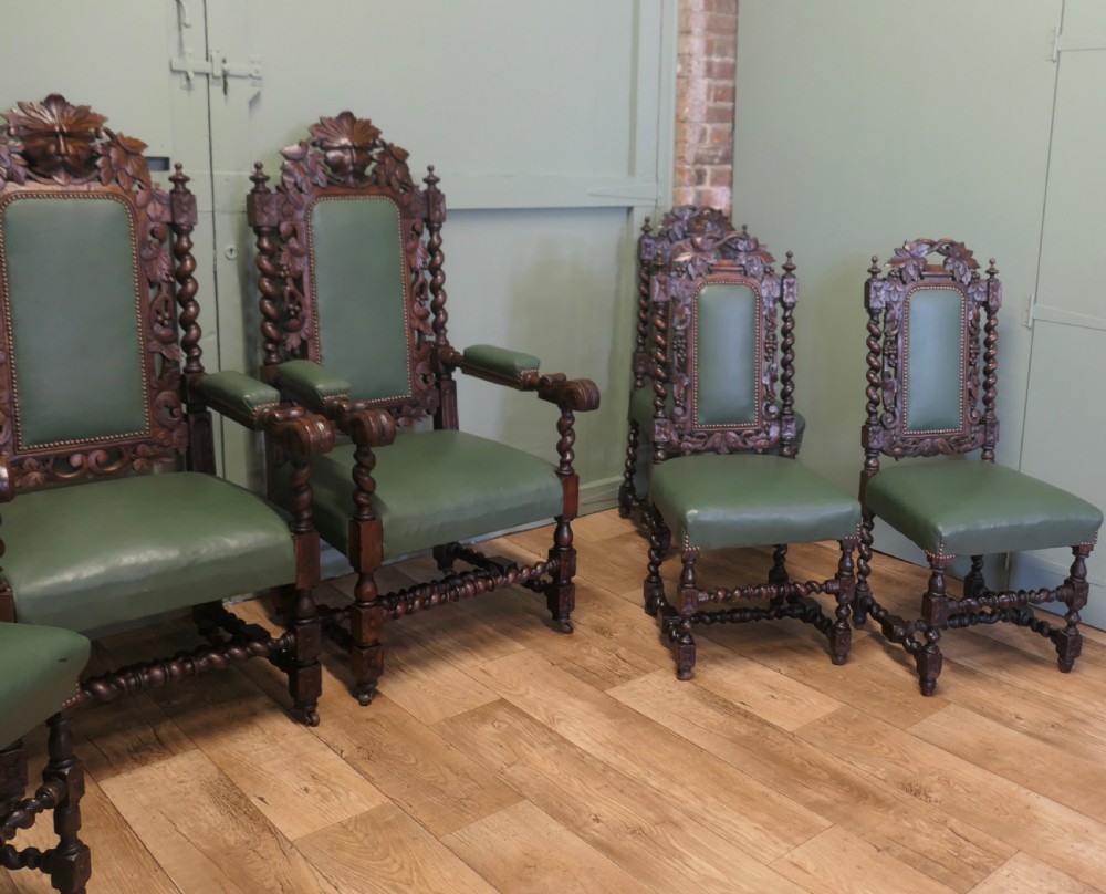 A set of ten carved oak dining chairs featuring green leather upholstery, barley twist legs, and detailed crest rails, comprising two carver armchairs and eight side chairs. View V
