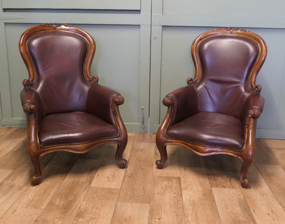 A pair of Victorian spoon back armchairs with carved mahogany frames, deep brown leather upholstery, and cabriole front legs. View II