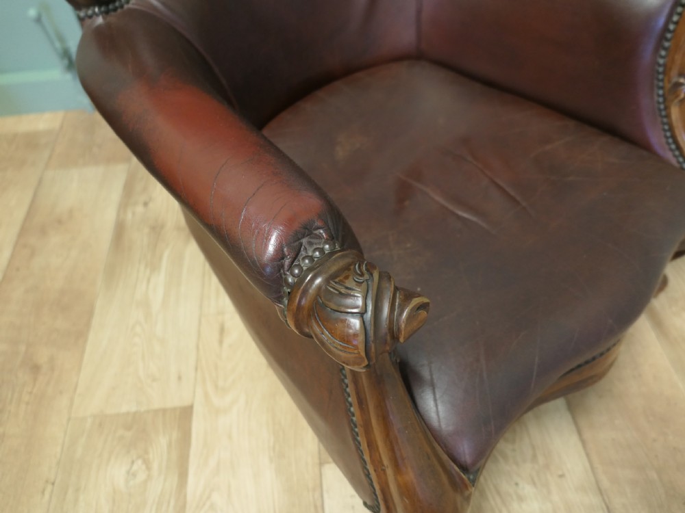 A pair of Victorian spoon back armchairs with carved mahogany frames, deep brown leather upholstery, and cabriole front legs. View V