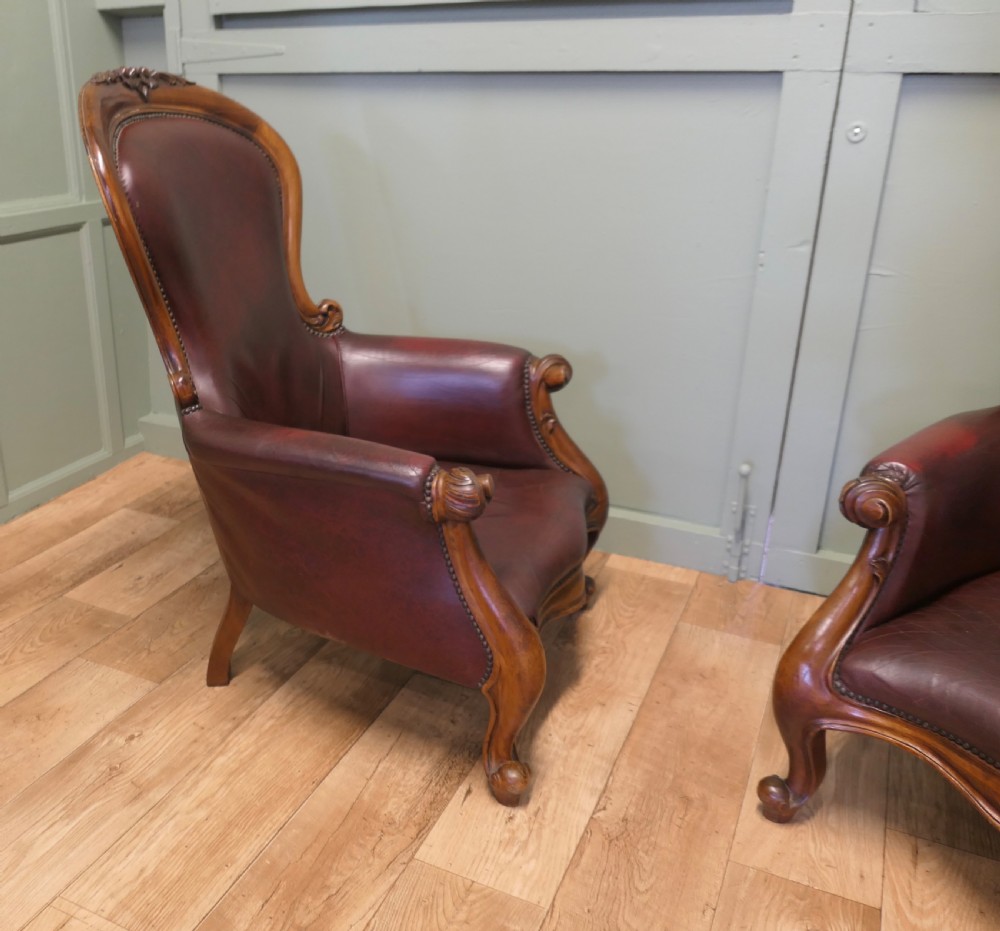 A pair of Victorian spoon back armchairs with carved mahogany frames, deep brown leather upholstery, and cabriole front legs. View VI