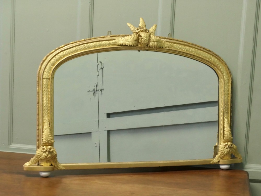 An arched gold giltwood overmantel mirror with fern leaf cresting and small corner feet.