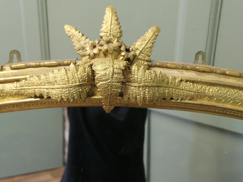 An arched gold giltwood overmantel mirror with fern leaf cresting and small corner feet. View III