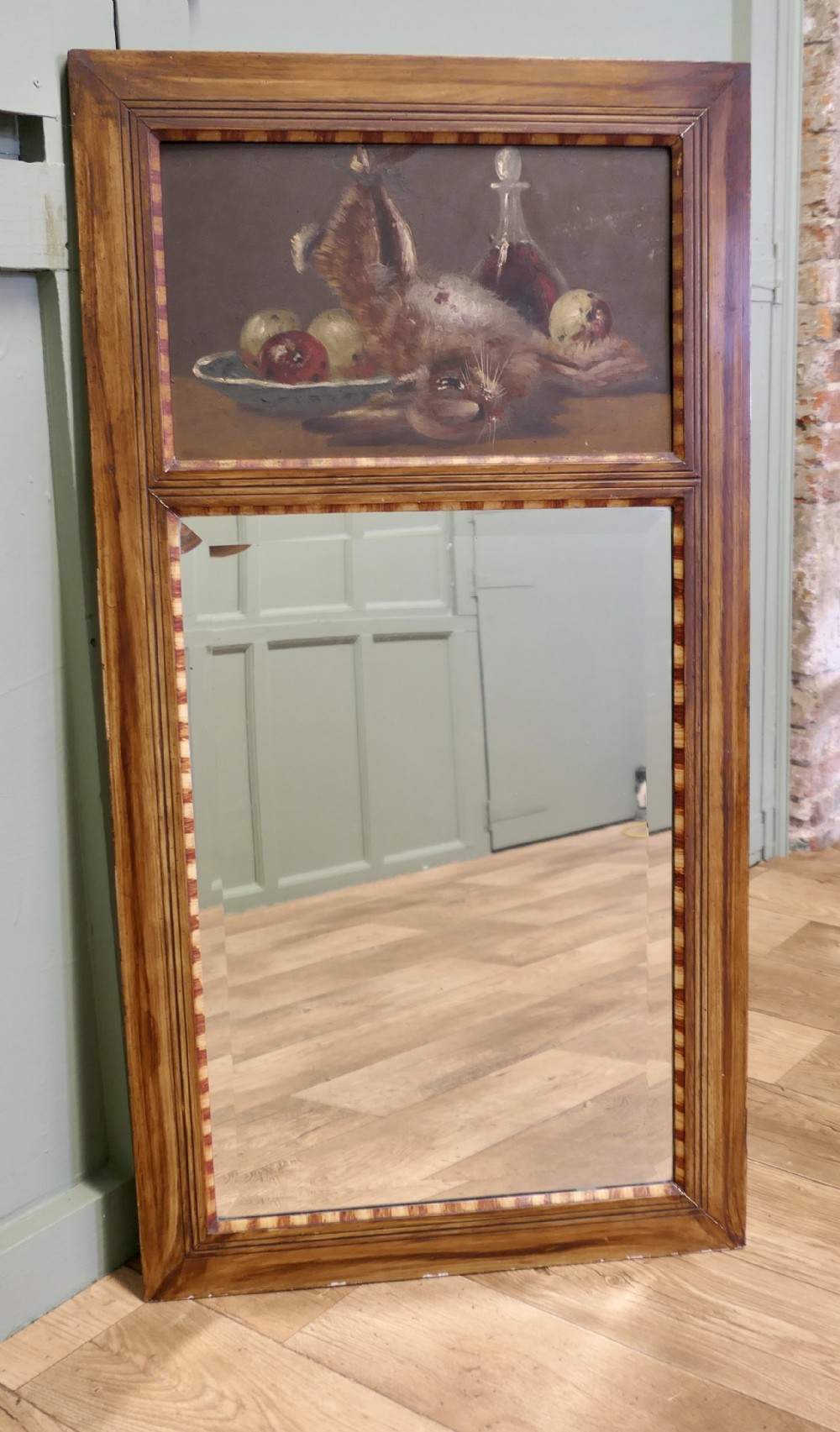 A tall rectangular timber-framed trumeau mirror featuring an inset oil painting of a game still life above a mirror panel.