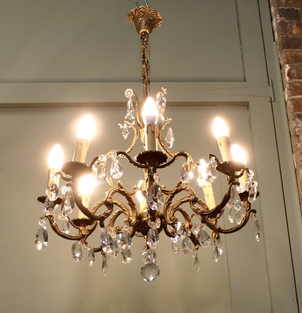 An ornate multi-arm French brass chandelier fitted with candle-effect bulbs and decorated with faceted crystal drop lustres.