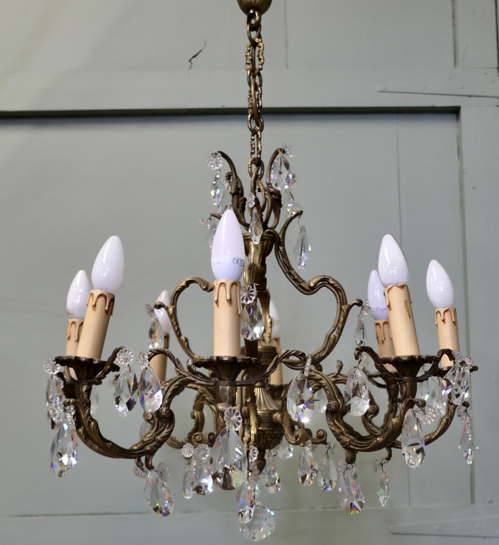 An ornate multi-arm French brass chandelier fitted with candle-effect bulbs and decorated with faceted crystal drop lustres. View II