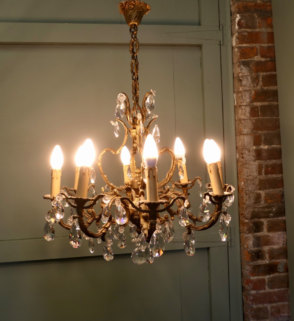 An ornate multi-arm French brass chandelier fitted with candle-effect bulbs and decorated with faceted crystal drop lustres. View V