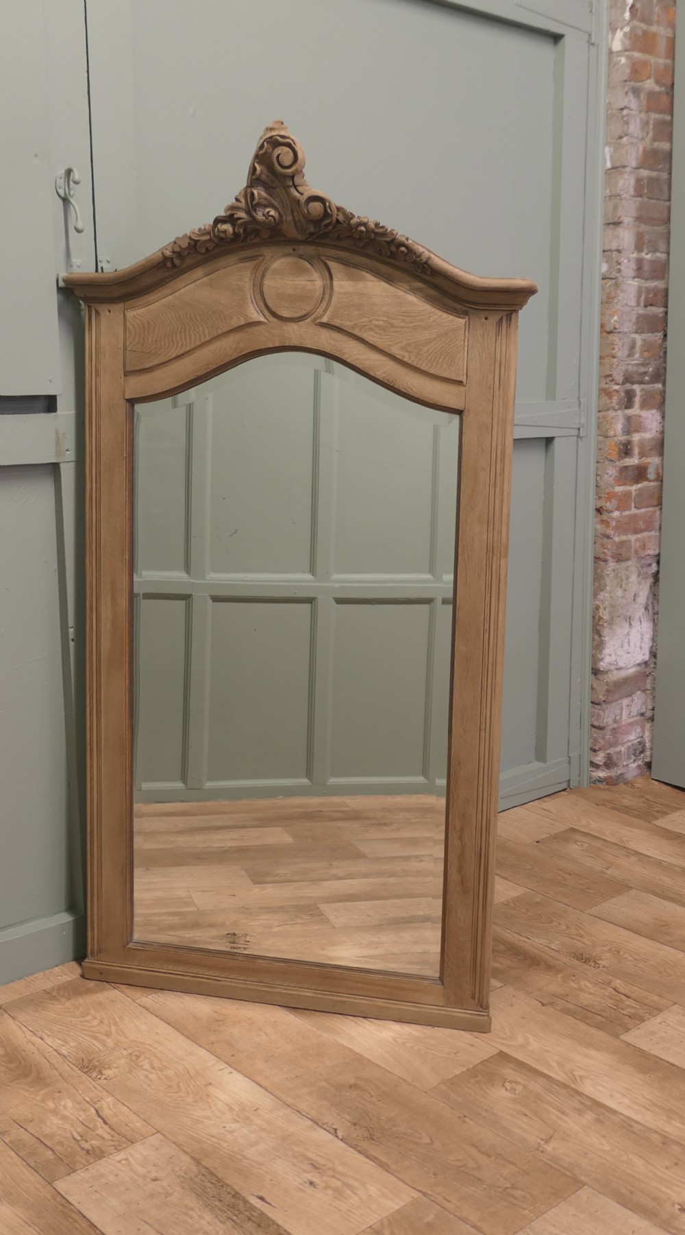 A tall French Provincial style wall mirror with a bleached oak arched frame and a detailed hand-carved floral crest.