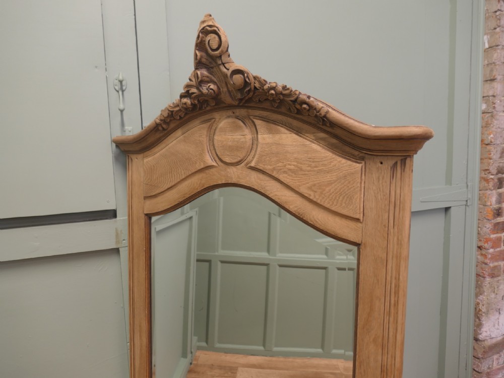 A tall French Provincial style wall mirror with a bleached oak arched frame and a detailed hand-carved floral crest. View VI
