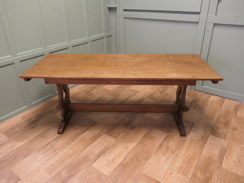 An Arts and Crafts solid golden oak refectory dining table featuring shaped trestle end supports and a central connecting stretcher. View II