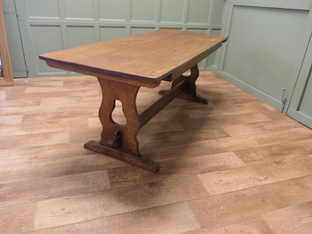 An Arts and Crafts solid golden oak refectory dining table featuring shaped trestle end supports and a central connecting stretcher. View III