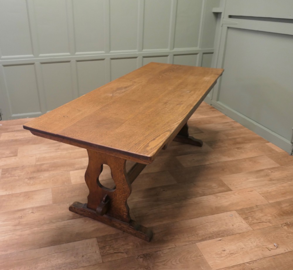 An Arts and Crafts solid golden oak refectory dining table featuring shaped trestle end supports and a central connecting stretcher. View IV