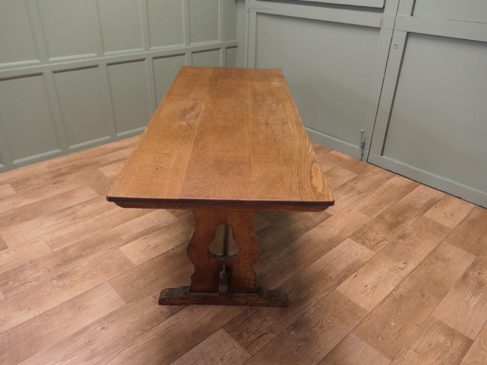 An Arts and Crafts solid golden oak refectory dining table featuring shaped trestle end supports and a central connecting stretcher. View V