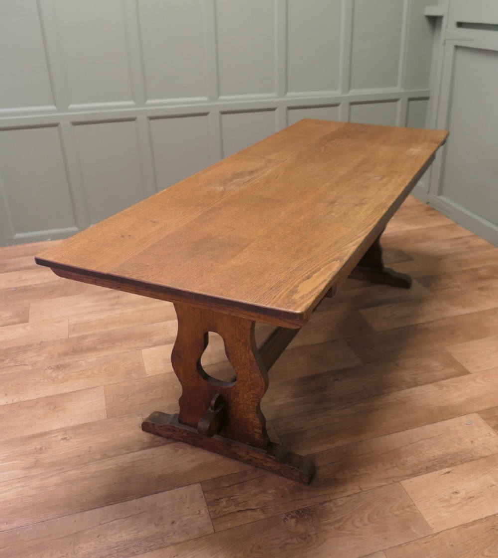 An Arts and Crafts solid golden oak refectory dining table featuring shaped trestle end supports and a central connecting stretcher. View VI