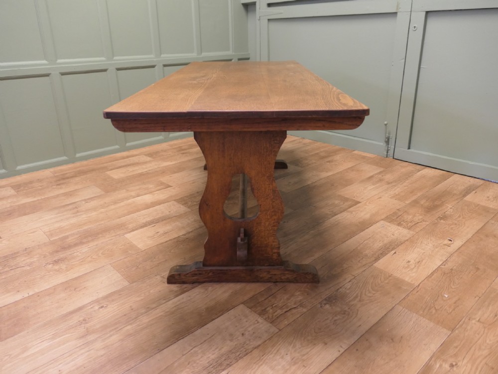 An Arts and Crafts solid golden oak refectory dining table featuring shaped trestle end supports and a central connecting stretcher. View VII