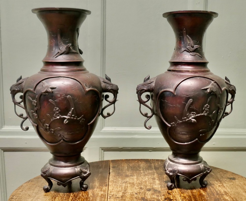 A pair of dark brown Japanese Meiji period bronze vases featuring relief depictions of birds on branches and dragon-shaped handles on footed bases.