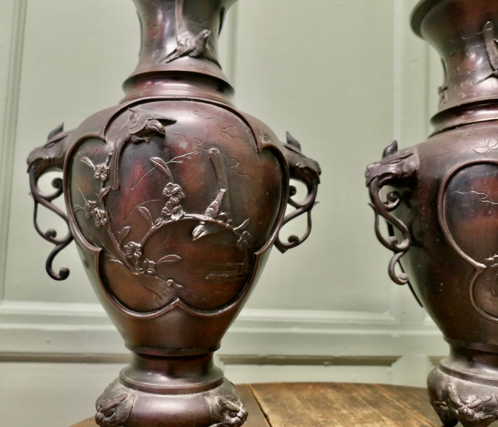 A pair of dark brown Japanese Meiji period bronze vases featuring relief depictions of birds on branches and dragon-shaped handles on footed bases. View IV