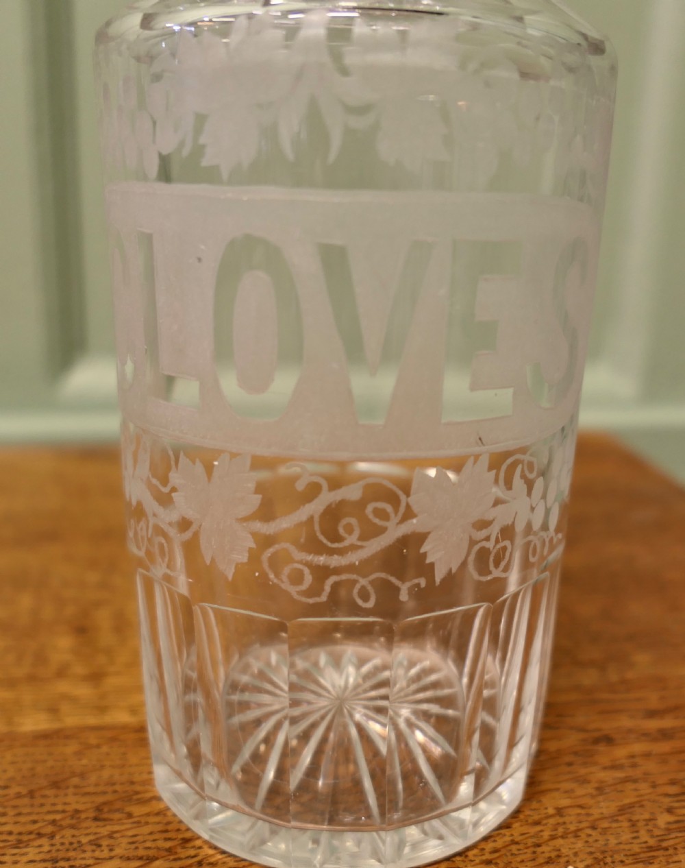 A Victorian clear crystal decanter featuring etched lettering spelling Cloves framed by vine motifs, complete with a fluted neck and faceted glass stopper. View III