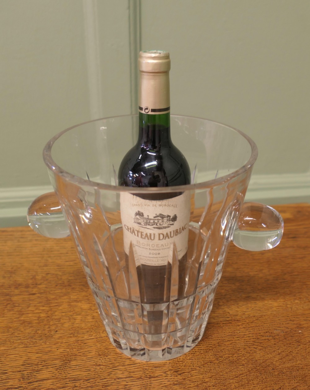 A clear hand-cut crystal ice bucket featuring geometric facets and two solid round side handles. View II