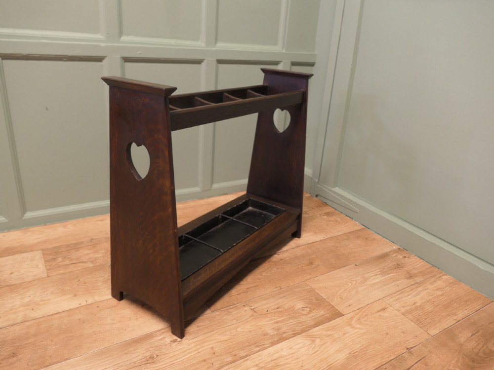 A dark oak Arts and Crafts umbrella stand featuring heart-shaped cutouts on sloped side panels and a metal drip tray at the base.