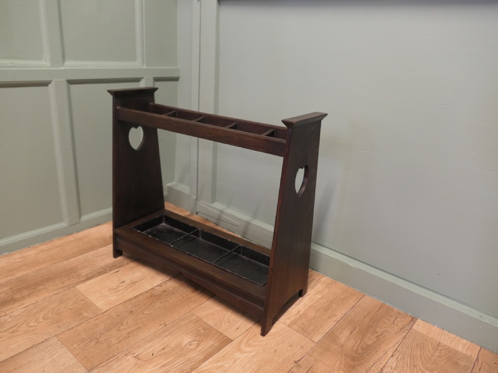 A dark oak Arts and Crafts umbrella stand featuring heart-shaped cutouts on sloped side panels and a metal drip tray at the base. View V