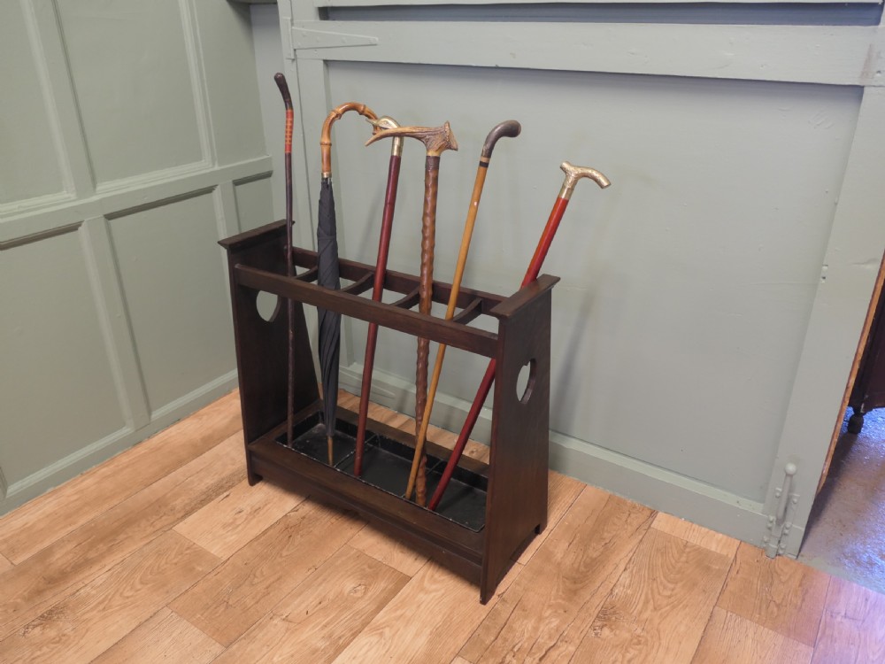 A dark oak Arts and Crafts umbrella stand featuring heart-shaped cutouts on sloped side panels and a metal drip tray at the base. View VI