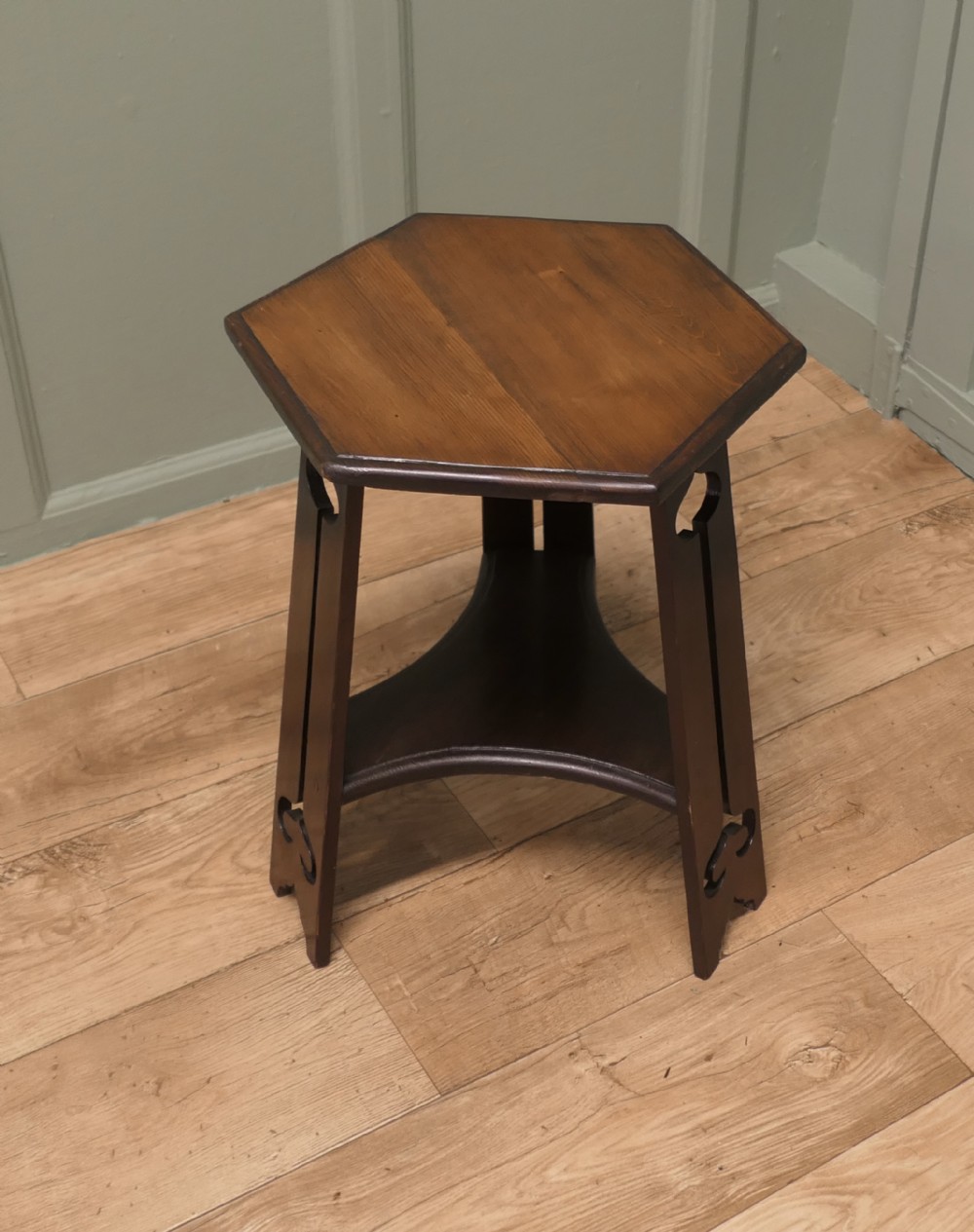 An Arts and Crafts wooden side table featuring a hexagonal top, three shaped legs with pierced cutouts, and a lower triangular stretcher.