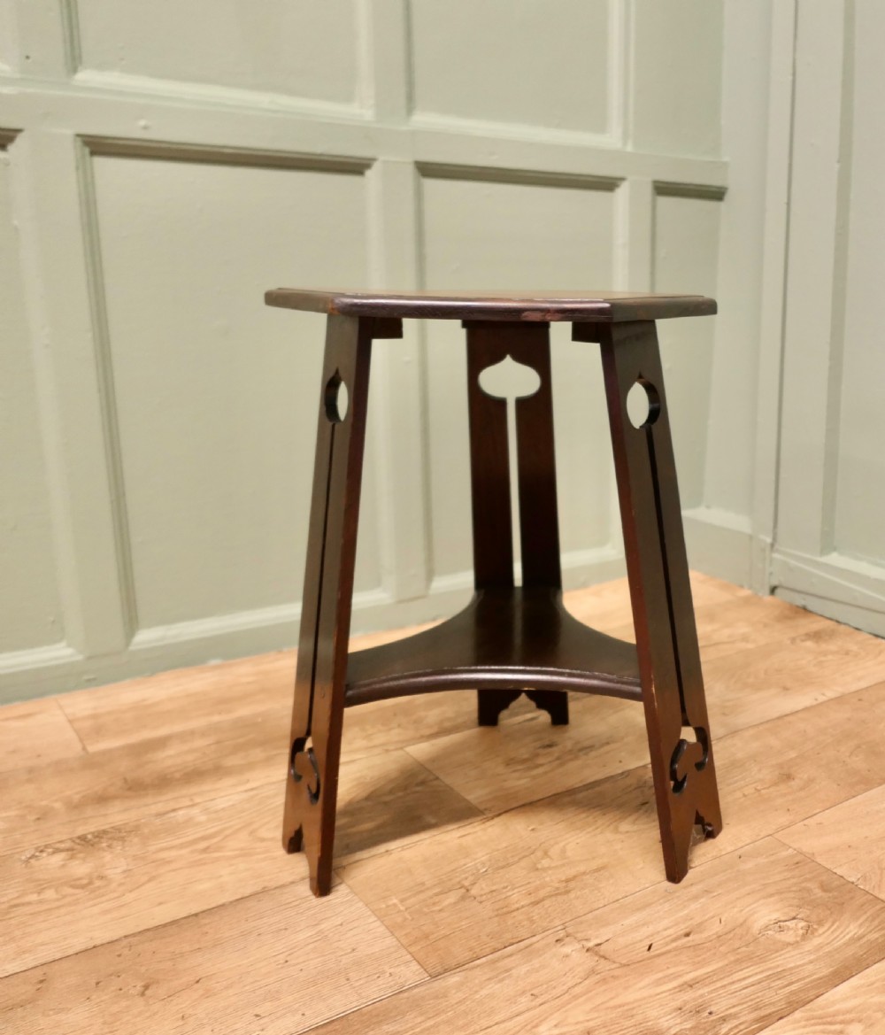 An Arts and Crafts wooden side table featuring a hexagonal top, three shaped legs with pierced cutouts, and a lower triangular stretcher. View II
