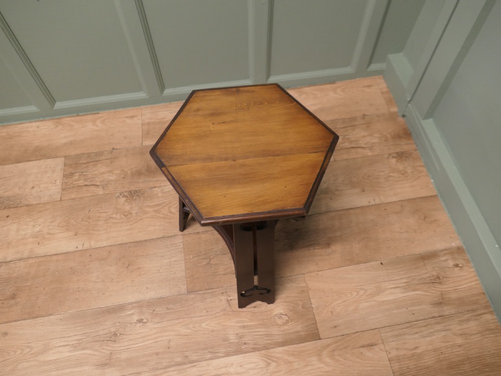 An Arts and Crafts wooden side table featuring a hexagonal top, three shaped legs with pierced cutouts, and a lower triangular stretcher. View IV