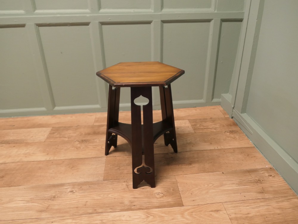 An Arts and Crafts wooden side table featuring a hexagonal top, three shaped legs with pierced cutouts, and a lower triangular stretcher. View V