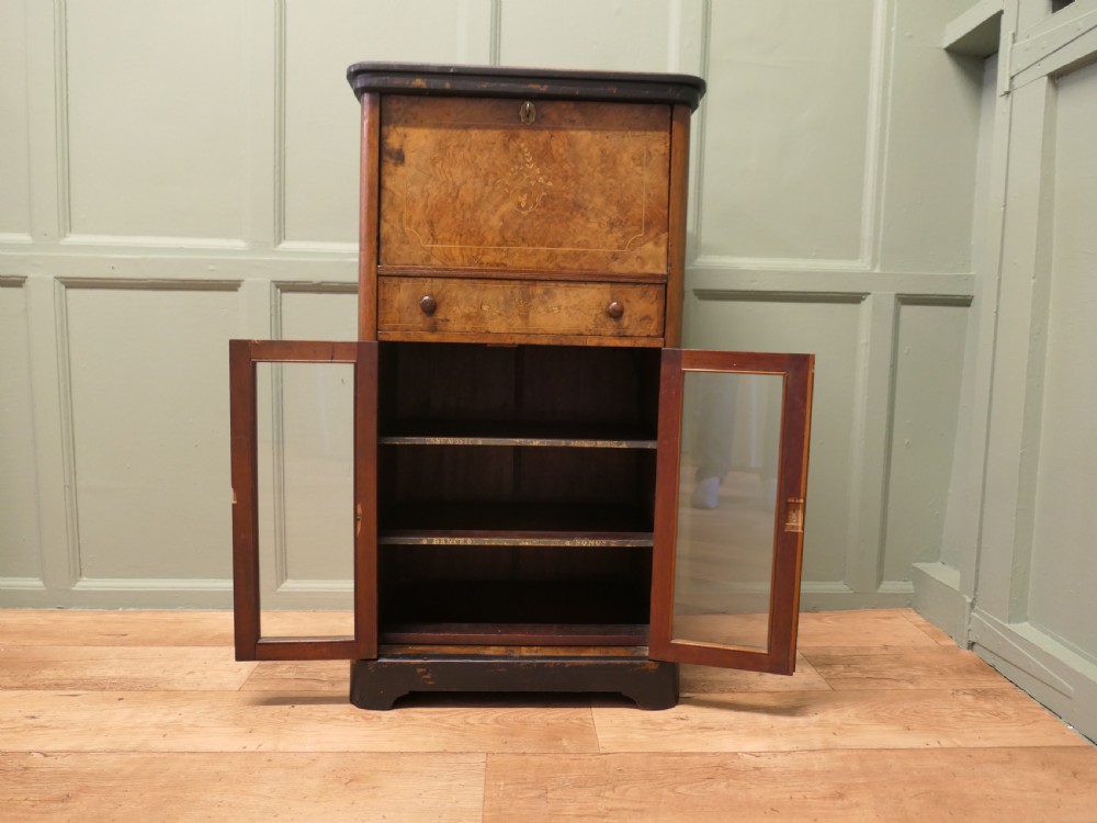 A Victorian burr walnut music filing cabinet featuring a fall-front upper compartment with inlaid details, a central drawer, and double glazed lower doors. View IV