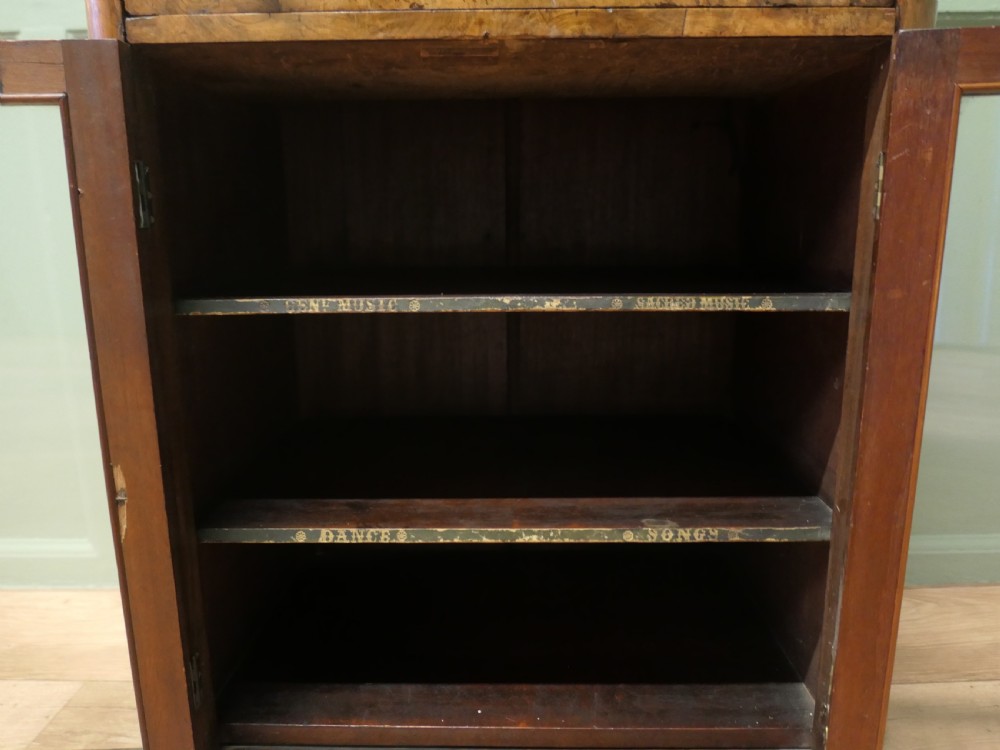 A Victorian burr walnut music filing cabinet featuring a fall-front upper compartment with inlaid details, a central drawer, and double glazed lower doors. View VI