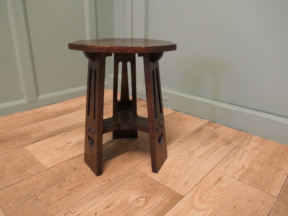 An octagonal Arts and Crafts solid oak plant stand featuring splayed legs with vertical slots and heart cut-outs connected by a lower stretcher.