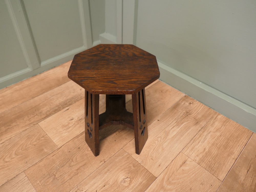 An octagonal Arts and Crafts solid oak plant stand featuring splayed legs with vertical slots and heart cut-outs connected by a lower stretcher. View II