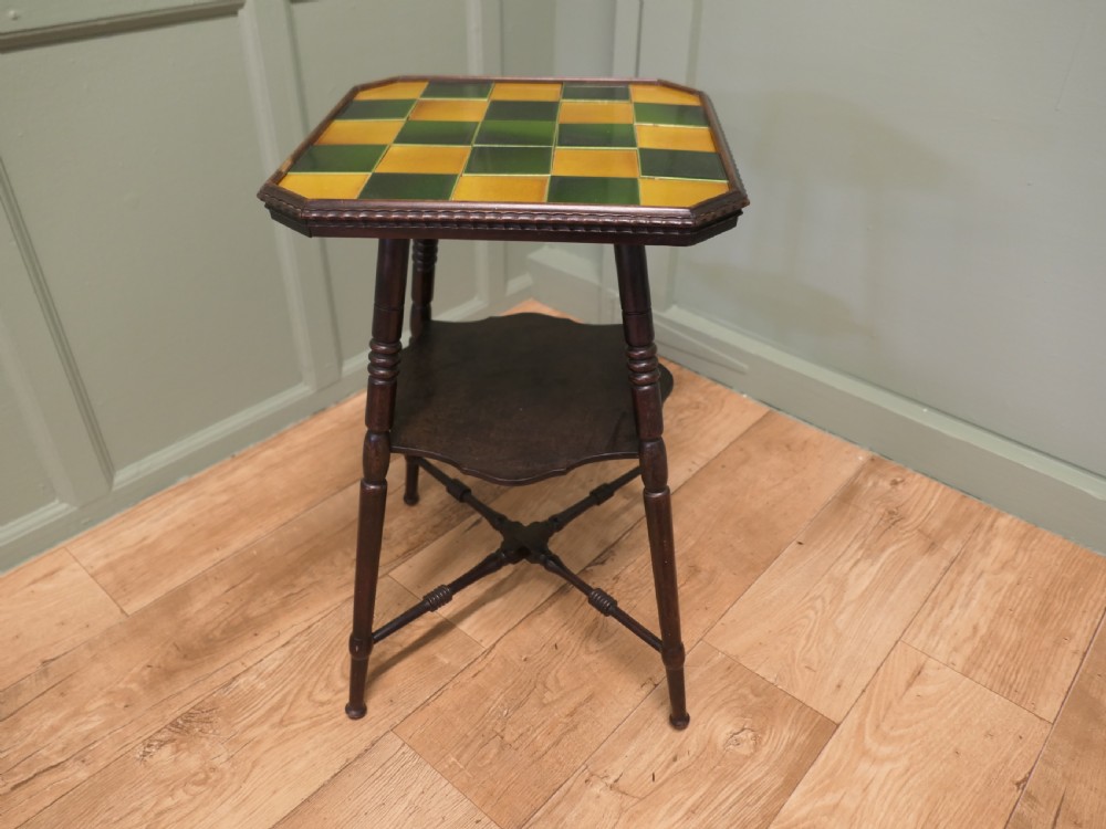 An Arts and Crafts dark wood side table with a chequerboard top made of green and yellow glazed ceramic tiles, turned legs, and an undertier. View II