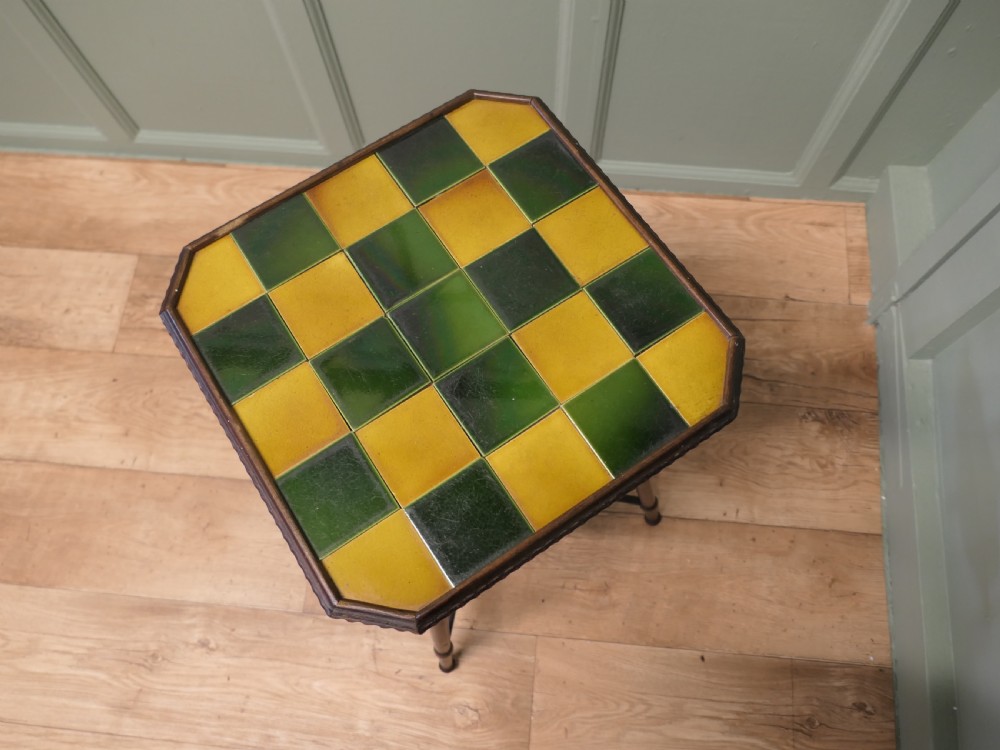 An Arts and Crafts dark wood side table with a chequerboard top made of green and yellow glazed ceramic tiles, turned legs, and an undertier. View VI