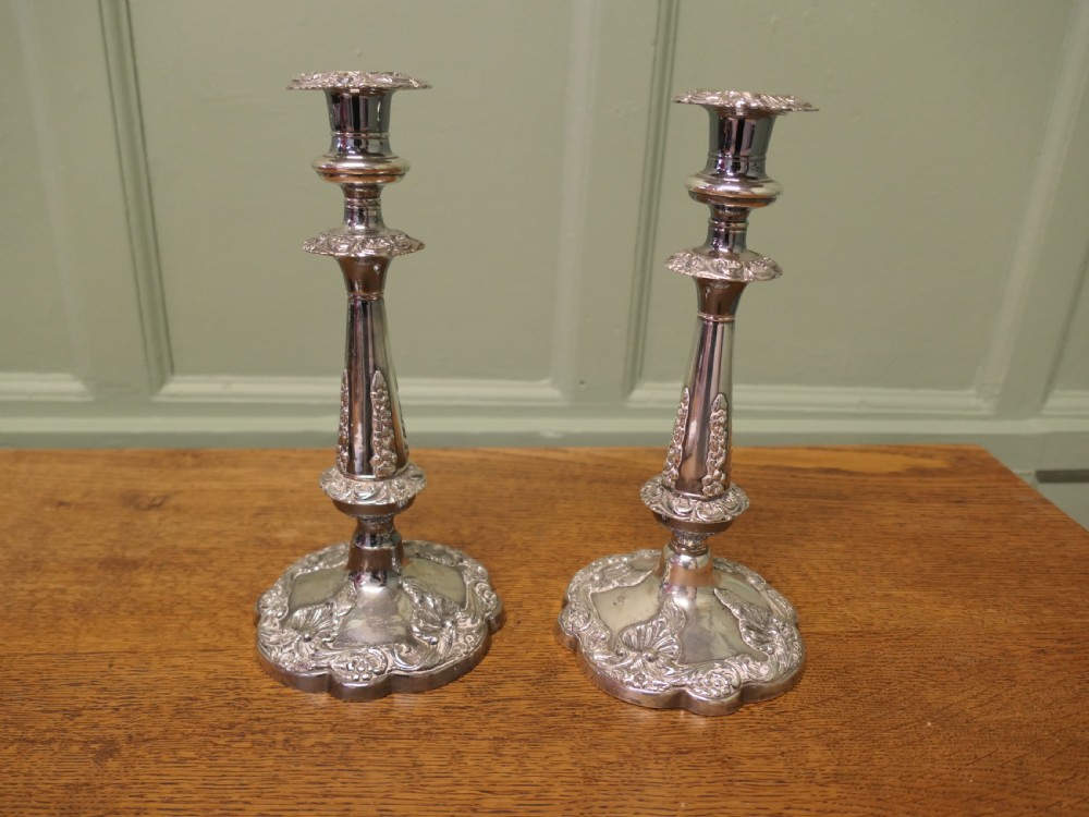 A pair of 19th-century silver-plated candlesticks featuring floral relief details on the shaped bases and tapered stems.