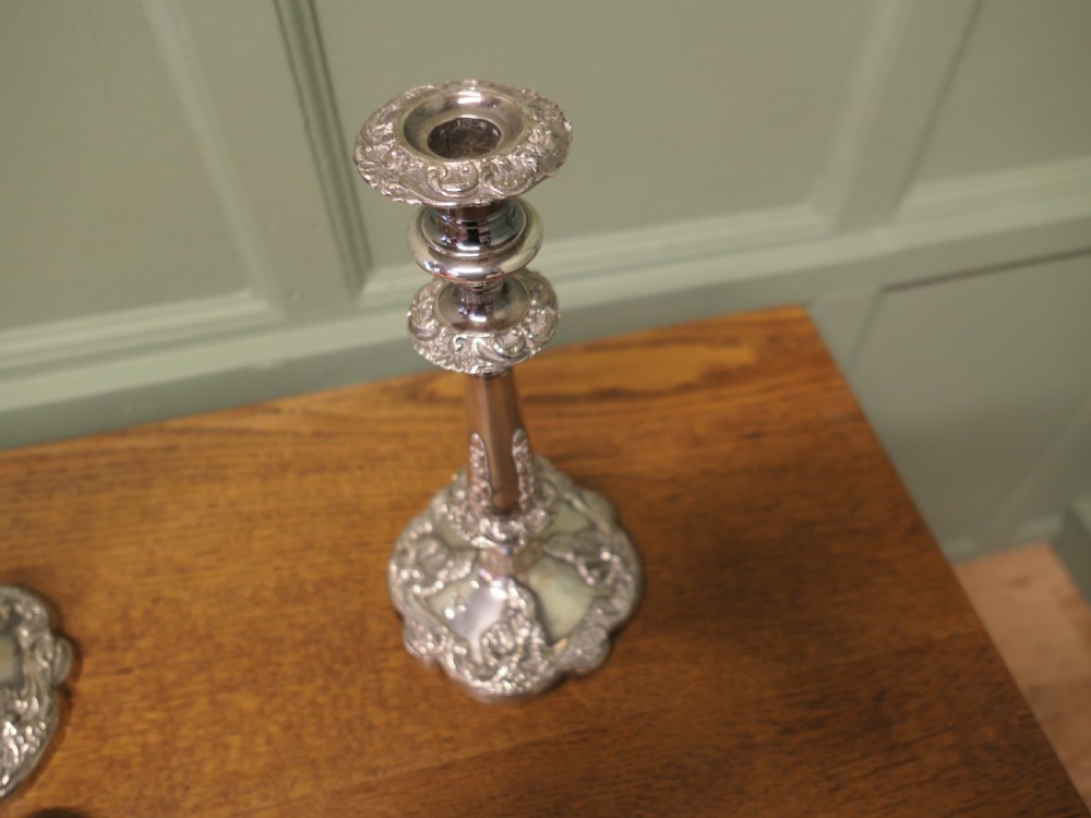 A pair of 19th-century silver-plated candlesticks featuring floral relief details on the shaped bases and tapered stems. View V