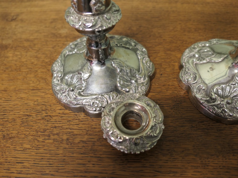 A pair of 19th-century silver-plated candlesticks featuring floral relief details on the shaped bases and tapered stems. View VII