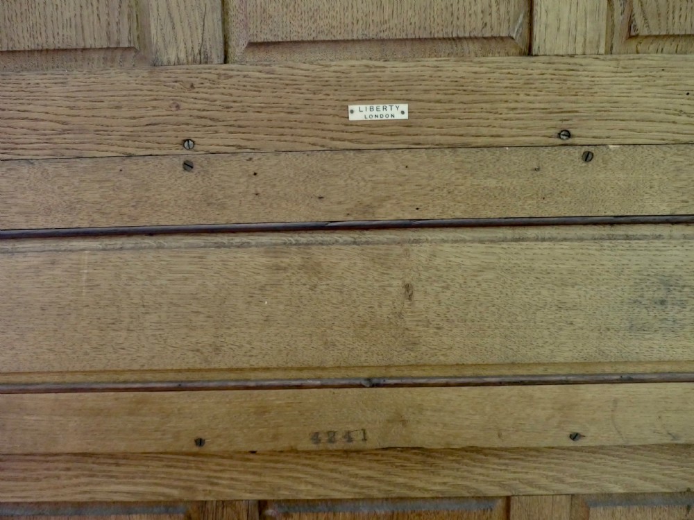A solid golden oak Arts and Crafts dresser featuring upper bullseye leaded glass doors with iron strap hinges above an open shelf and carved panelled lower doors. View VII