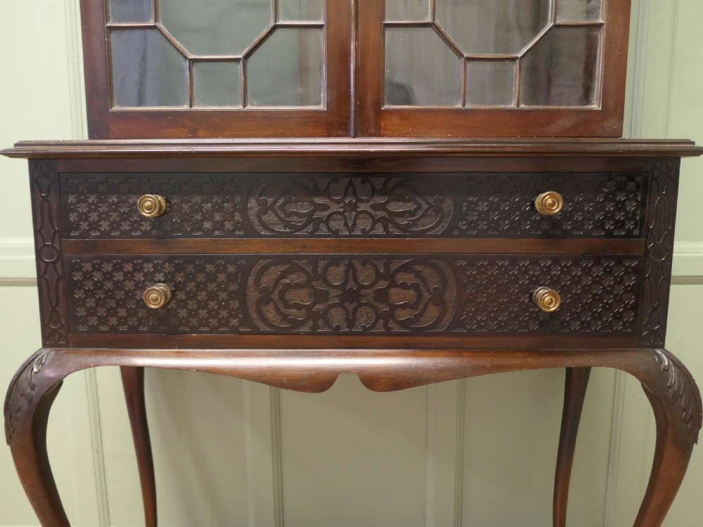 A mahogany Chinese Chippendale display cabinet featuring geometric astragal glazed doors, carved fretwork drawer fronts, and elevated slender cabriole legs. View III