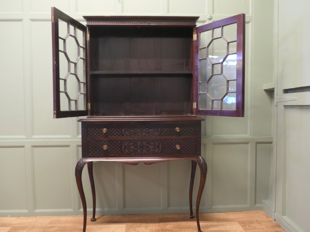 A mahogany Chinese Chippendale display cabinet featuring geometric astragal glazed doors, carved fretwork drawer fronts, and elevated slender cabriole legs. View V