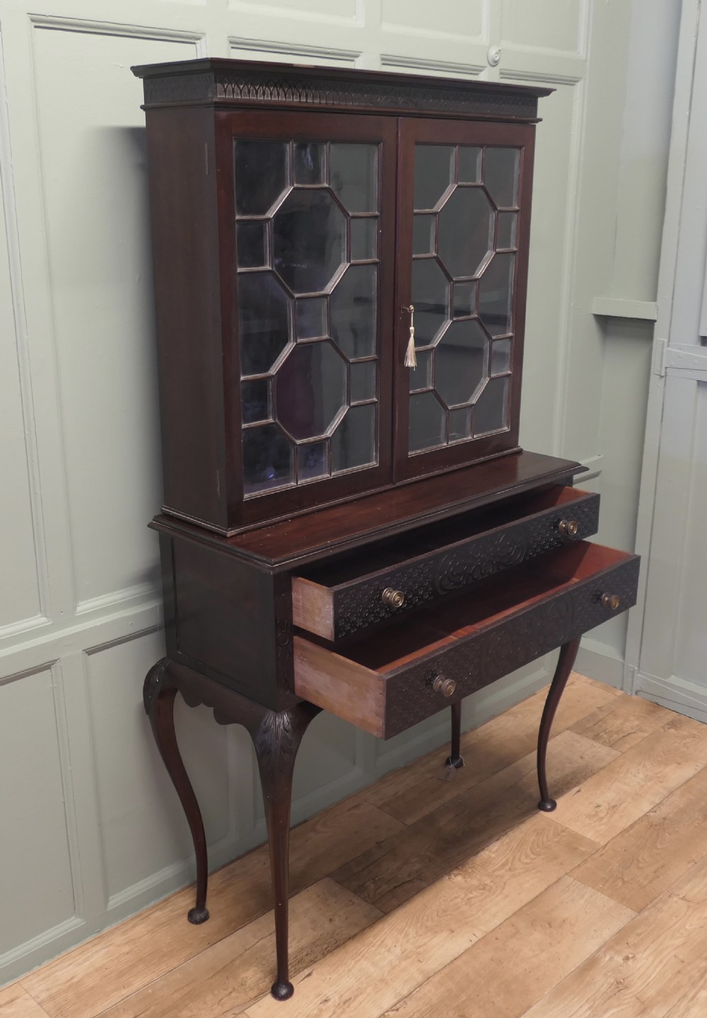 A mahogany Chinese Chippendale display cabinet featuring geometric astragal glazed doors, carved fretwork drawer fronts, and elevated slender cabriole legs. View VI