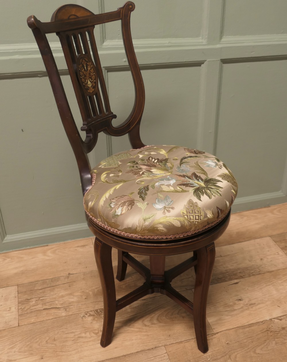An antique mahogany revolving music chair featuring a lyre-shaped backrest with inlaid urn motif, a round embroidered seat cushion, and four splayed legs with a central cross-stretcher. View II