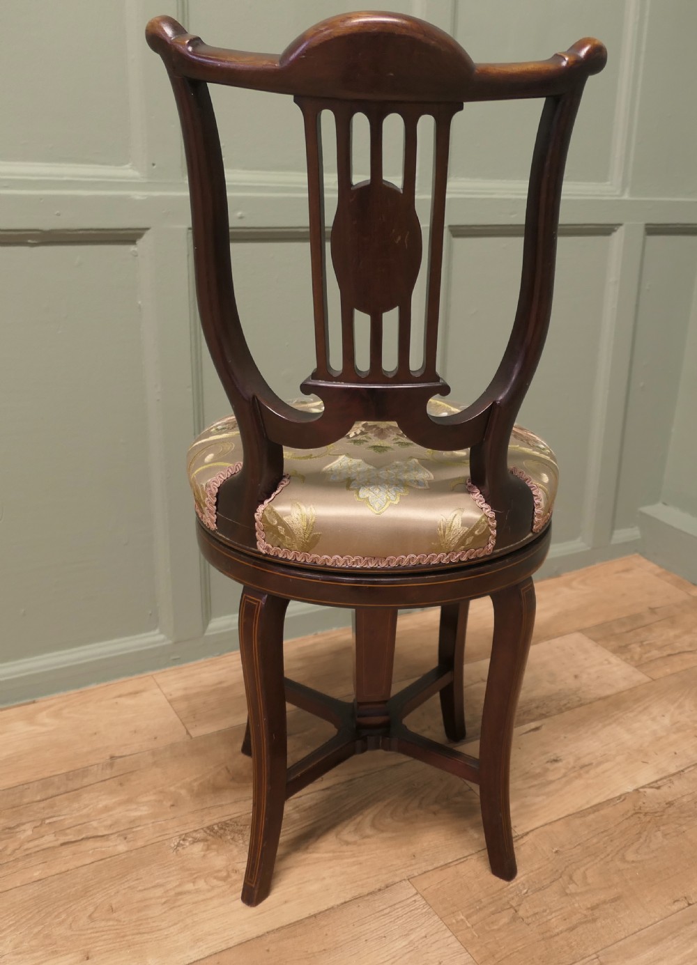 An antique mahogany revolving music chair featuring a lyre-shaped backrest with inlaid urn motif, a round embroidered seat cushion, and four splayed legs with a central cross-stretcher. View III