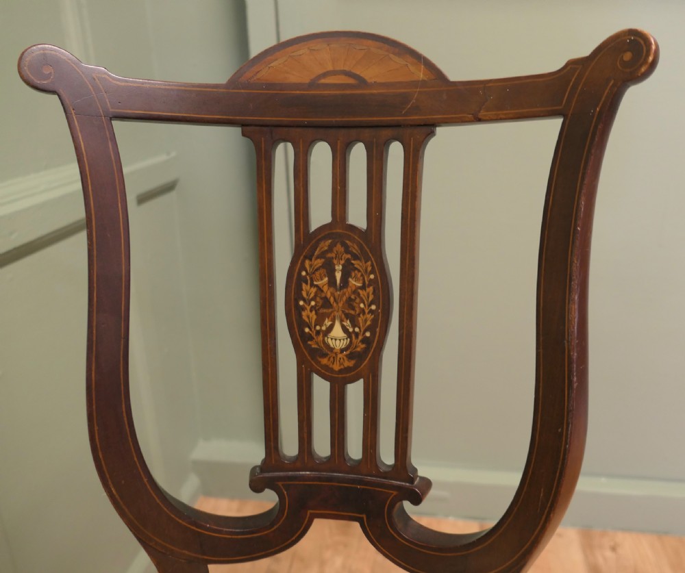 An antique mahogany revolving music chair featuring a lyre-shaped backrest with inlaid urn motif, a round embroidered seat cushion, and four splayed legs with a central cross-stretcher. View IV