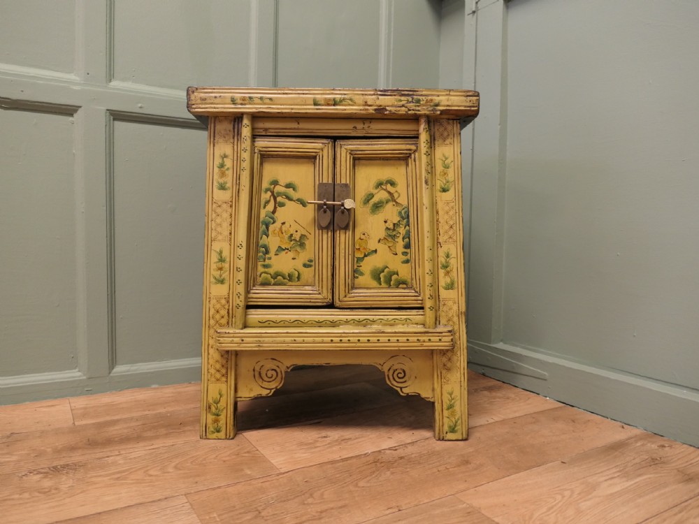 A nineteenth-century cream painted wooden Chinoiserie cabinet featuring two doors illustrated with Asian figures, foliage, decorative borders, and a brass pin closure.