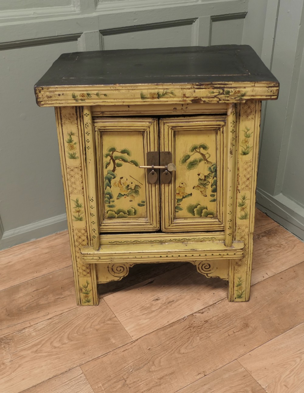 A nineteenth-century cream painted wooden Chinoiserie cabinet featuring two doors illustrated with Asian figures, foliage, decorative borders, and a brass pin closure. View II