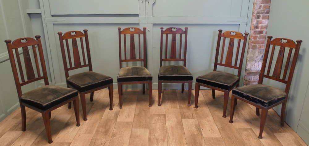 A set of six golden oak Arts and Crafts dining chairs featuring vertical slatted backs with top rail cutouts and dark green upholstered seats.