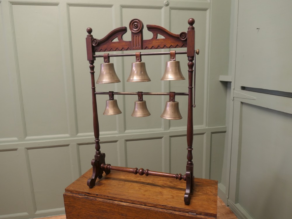 A Victorian carved walnut rack displaying six tuned brass bells arranged across two horizontal tiers on turned wooden uprights.